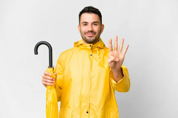 年轻的高加索人 穿着防雨外套 带着雨伞 高高兴兴地盖在孤立的白色背景上 用手指数着四个人 — 图库照片