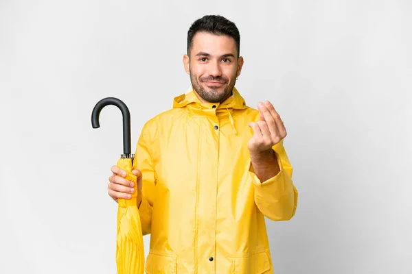 若いですCaucasian男とともに防水コートと傘上の隔離されたホワイトバックグランド作るお金ジェスチャー — ストック写真