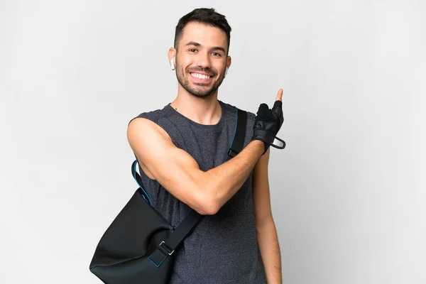 stock image Young sport caucasian man with sport bag over over isolated white background pointing back