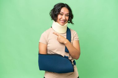 Arjantinli genç bir kadın boyunluk takıyor ve izole edilmiş arka planda asılı duruyor. Ürünü sunmak için yan tarafı işaret ediyor.