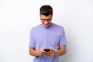 Beyaz arka planda izole edilmiş genç beyaz bir adam cep telefonuyla mesaj gönderiyor.