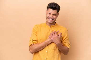 Young caucasian man isolated on beige background having a pain in the heart