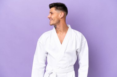 Young caucasian man doing karate isolated on purple background looking side