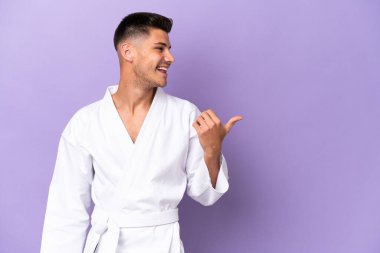 Mor arka planda karate yapan genç beyaz adam bir ürünü sunmak için yan tarafı işaret ediyor.