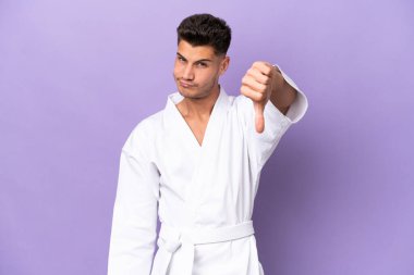 Mor arka planda karate yapan genç beyaz adam olumsuz ifade ile baş parmağını aşağı gösteriyor.