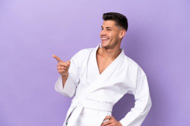 Mor arka planda karate yapan beyaz bir genç parmak göstererek bir ürün sunuyor.