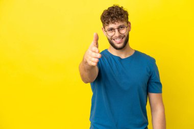 Sarı arka planda izole edilmiş yakışıklı beyaz adam iyi bir anlaşma için el sıkışıyor.