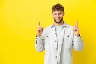 Sarı arka planda izole edilmiş yakışıklı beyaz adam harika bir fikre işaret ediyor.