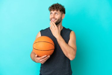 Basketbol oynayan yakışıklı genç adam mavi arka planda izole edilmiş gülümserken yukarı bakıyor.