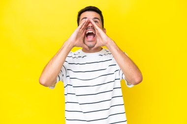 Izole sarı arka plan üzerinde genç yakışıklı adam bağırarak ve bir şey ilan
