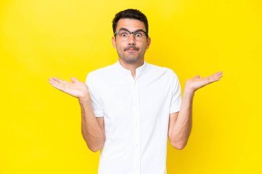 El kaldırırken şüpheleri olan izole sarı arka plan üzerinde genç yakışıklı adam