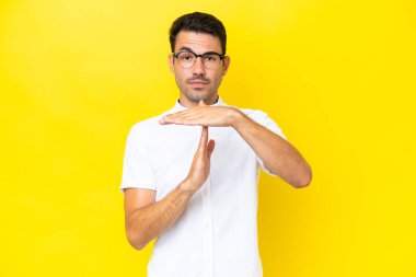 Soyutlanmış sarı arka planda genç yakışıklı bir adam zaman aşımı hareketi yapıyor.