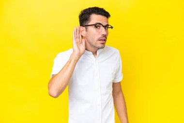Izole sarı arka plan üzerinde genç yakışıklı adam kulak elini koyarak bir şey dinlerken