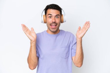 Soyutlanmış beyaz arka planı olan yakışıklı genç adam şaşırdı ve müzik dinliyor.