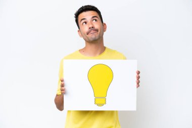 İzole edilmiş beyaz arka plan üzerinde genç yakışıklı bir adam elinde ampul simgesi olan bir pankart tutuyor ve yukarı bakıyor.