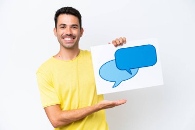 İzole edilmiş beyaz arka plan üzerinde genç yakışıklı bir adam elinde mutlu bir ifadeyle konuşma baloncuğu ikonu olan bir levha tutuyor.