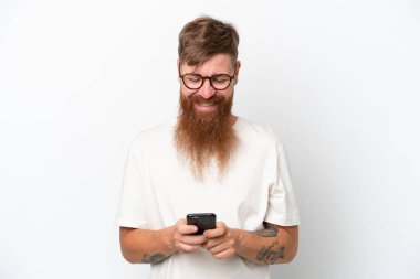 Uzun sakallı kızıl saçlı adam beyaz arka planda izole edilmiş. Cep telefonuyla mesaj yolluyor.