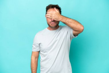 Orta yaşlı, beyaz bir adam mavi arka planda tek başına, gözleri elle kapatıyor. Bir şey görmek istemiyorum.