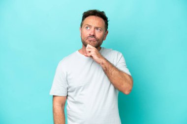 Orta yaşlı beyaz bir adam mavi arka planda izole edilmiş ve yukarı bakıyor.