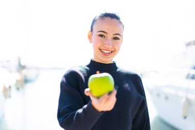 Açık havada elinde elmayla mutlu bir ifadeyle Faslı genç bir kız.