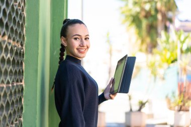 Genç Faslı kız elinde tabletle dışarıda gülümsüyor.