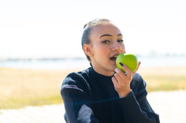 Dışarıda elinde elma tutan Faslı genç bir kız.