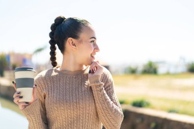 Faslı genç bir kız açık havada kahvesini yudumlarken bir fikir üretiyor ve etrafına bakıyor.