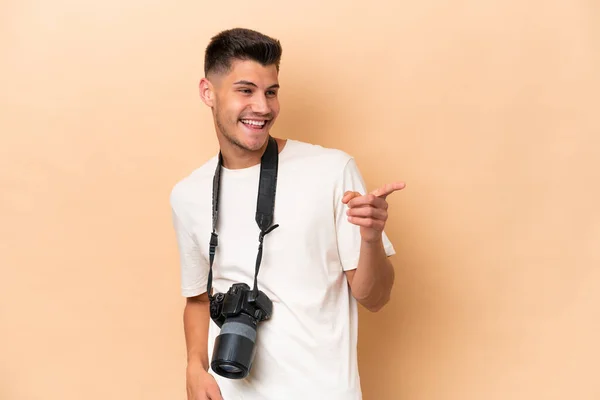 Mladý Fotograf Běloch Izolovaný Béžovém Pozadí Ukazující Prstem Stranu Prezentující — Stock fotografie