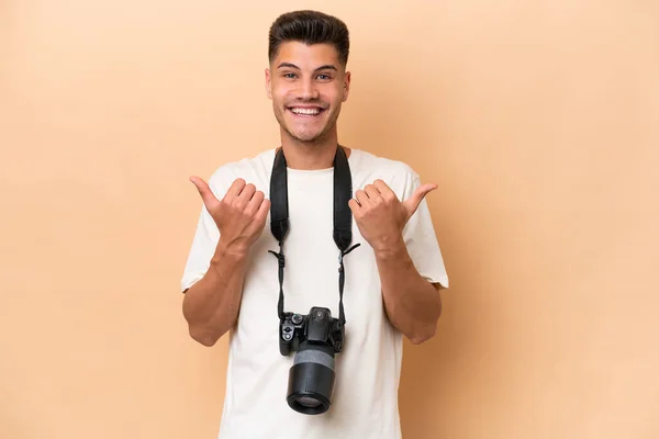 年轻的摄影师高加索人 背景是米黄色的 有大拇指 手势和微笑 — 图库照片