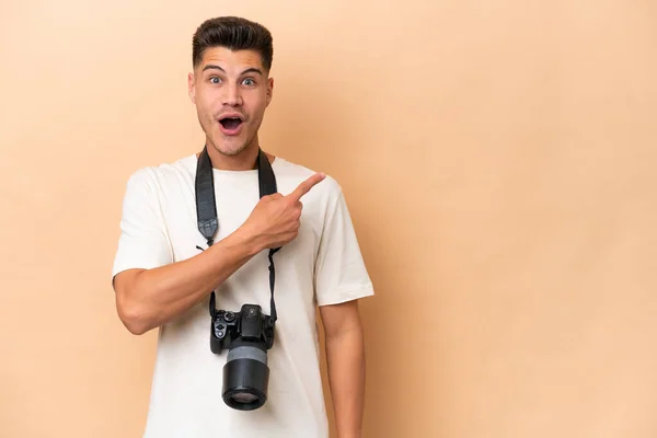 Young Photographer Caucasian Man Isolated Beige Background Surprised Pointing Side — Stock Photo, Image