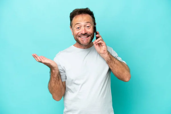 Middle age caucasian man isolated on blue background keeping a conversation with the mobile phone with someone