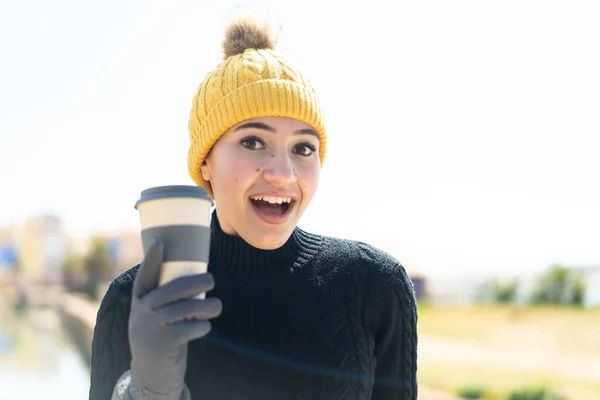 年轻的摩洛干姑娘穿着冬衣 在户外端着咖啡 脸上带着惊讶和震惊的表情 — 图库照片