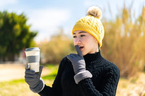 Young moroccan girl wearing winter muffs while holding a coffee at outdoors with surprise and shocked facial expression