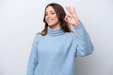 Beyaz arka planda izole edilmiş genç beyaz kadın parmaklarıyla tamam işareti gösteriyor.