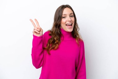 Beyaz arka planda izole edilmiş genç beyaz kadın gülümsüyor ve zafer işareti gösteriyor.