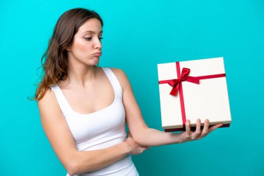 Mavi arka planda hüzünlü bir ifadeyle izole edilmiş bir hediye tutan beyaz bir kadın.