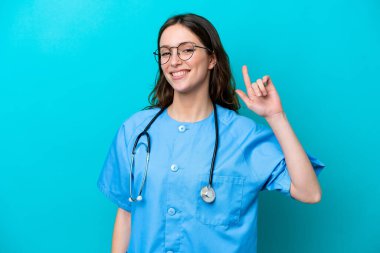 Genç cerrah kadın doktor mavi arka planda izole edildi ve en iyinin işareti olarak parmağını kaldırdı.