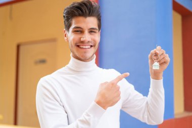 Kafkasyalı genç bir adam evinin anahtarlarını açık havada tutuyor ve ona doğrultuyor.