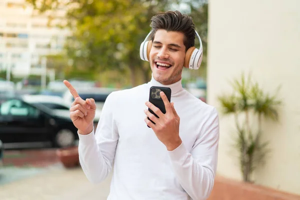 stock image Young caucasian man at outdoors listening music with a mobile and singing