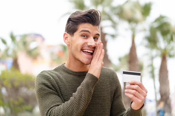 Young Caucasian Man Holding Credit Card Outdoors Whispering Something — Stock Photo, Image