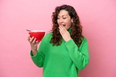 Beyaz bir kadın elinde bir kase mısır gevreği tutuyor. Pembe arka planda, şaşırmış ve şok olmuş bir yüz ifadesi var.