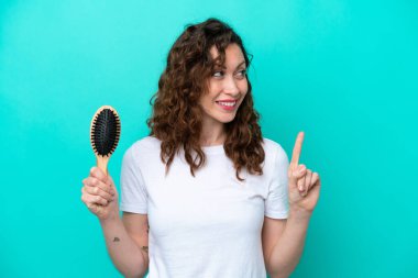 Mavi arka planda saç fırçası tutan beyaz bir kadın çözümü bulmak için parmağını kaldırıyor.