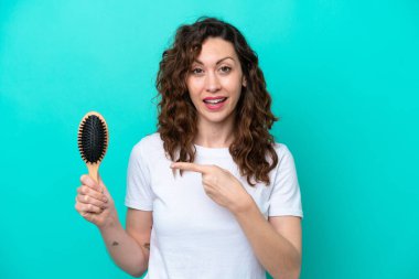 Mavi arka planda saç fırçası tutan beyaz bir kadın var.