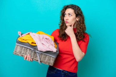 Mavi arka planda izole edilmiş çamaşır sepetini tutan beyaz bir kadın şüpheleri var.