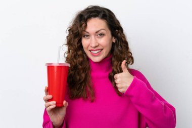 Young caucasian woman drinking soda isolated on white background with thumbs up because something good has happened