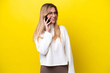 Genç Uruguaylı kadın sarı arka planda izole edilmiş cep telefonuyla biriyle sohbet ediyor.