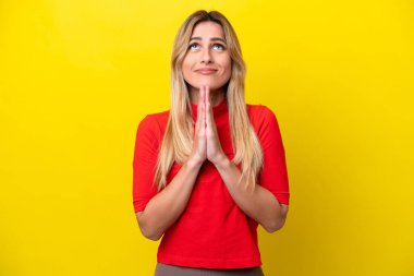 Sarı arka planda izole edilmiş genç Uruguaylı kadın avuç içlerini bir arada tutuyor. İnsan bir şey ister.