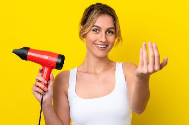 Uruguaylı genç bir kadın elinde saç kurutma makinesiyle Don sarı arka planı izole ediyor. Bizimle gelmesi için davet ediyor. Gelmene sevindim.