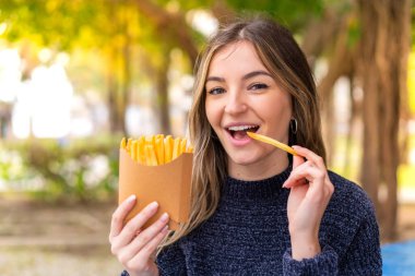 Genç ve güzel Romen kadın açık havada patates kızartması tutuyor.