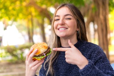 Genç, güzel Romen kadın elinde bir hamburgerle onu işaret ediyor.